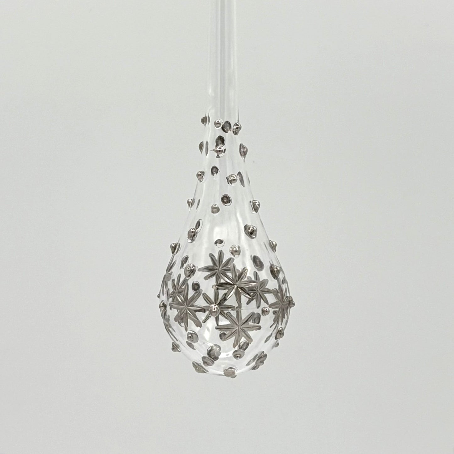 Clear handblown glass teardrop-shaped ornament with star-like platinum colored decorations