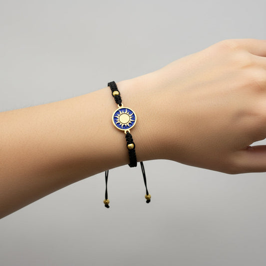 Black macrame bracelet with a brass medallion featuring a gold sun emblem on blue enamel