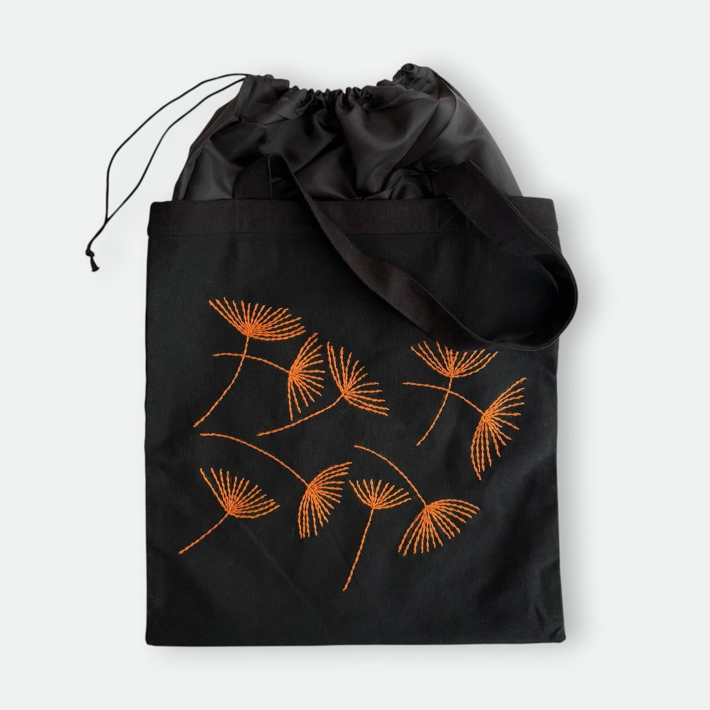 Black canvas tote bag with hand-embroidered orange papyrus design and drawstring lining, fair trade handmade