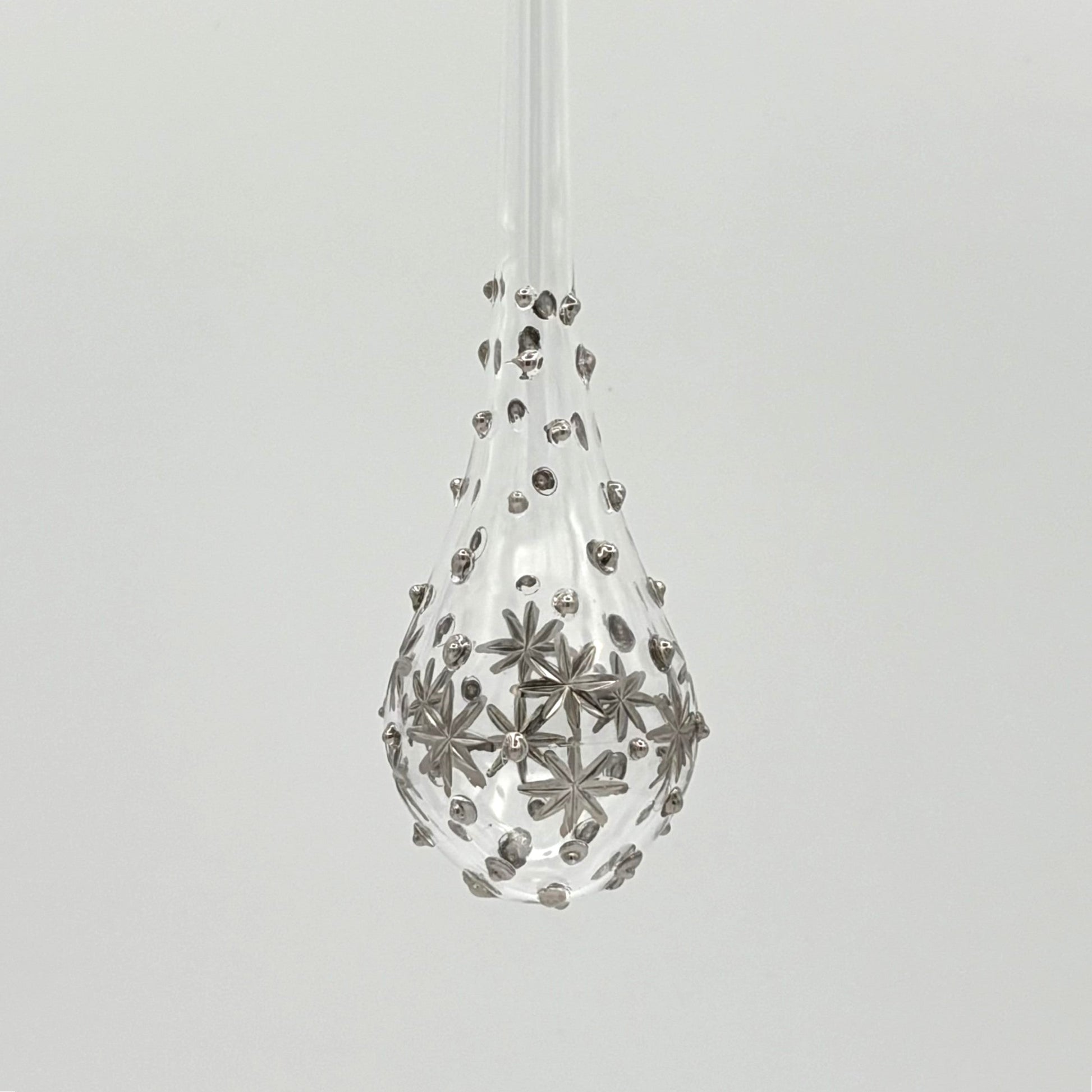 Clear handblown glass teardrop-shaped ornament with star-like platinum colored decorations 