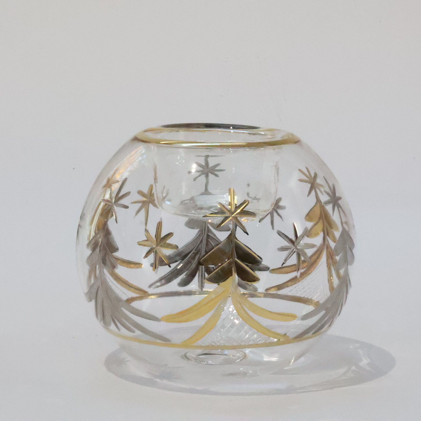 A hand blown glass tealight candle holder with gold and silver Christmas tree decorations 