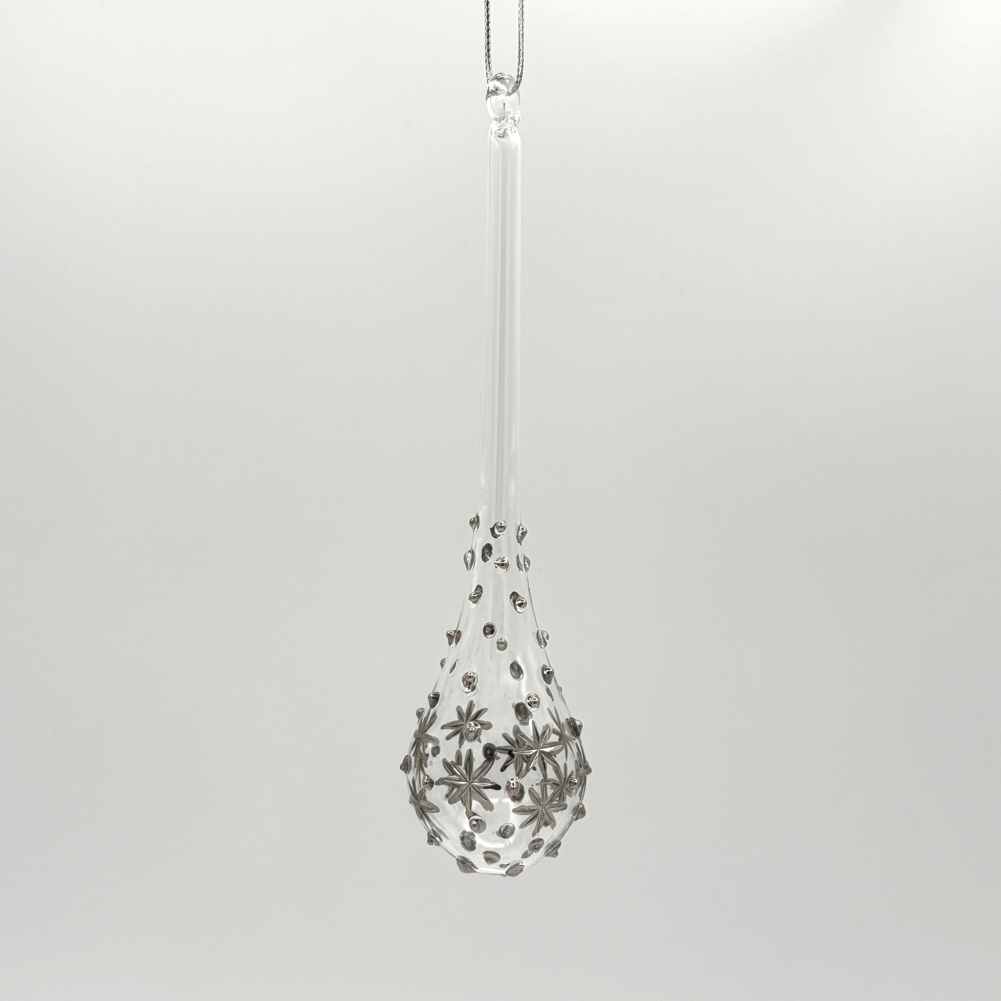 Clear handblown glass teardrop-shaped ornament with star-like platinum colored decorations 