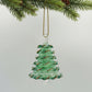 Green blown glass Christmas tree ornament hanging from a branch with pine cones.