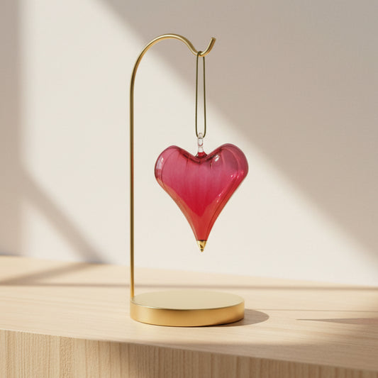 Heart-shaped hand-blown glass red ornament with gold tip hanging from a gold branch 