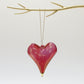 Heart-shaped hand-blown glass red ornament with gold tip hanging from a gold branch 