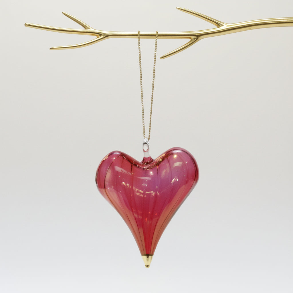 Heart-shaped hand-blown glass red ornament with gold tip hanging from a gold branch 