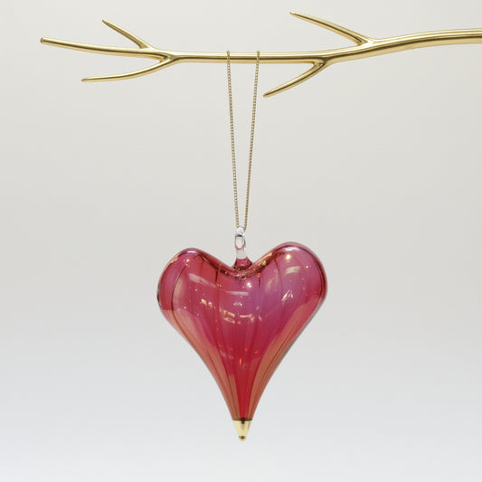 Heart-shaped hand-blown glass red ornament with gold tip hanging from a gold branch 