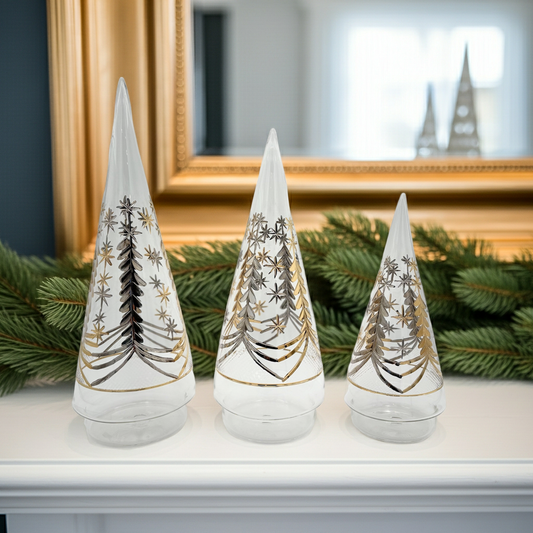 Three decorative blown glass Christmas trees with tree engraved patterns in gold and silver on a mantelpiece.
