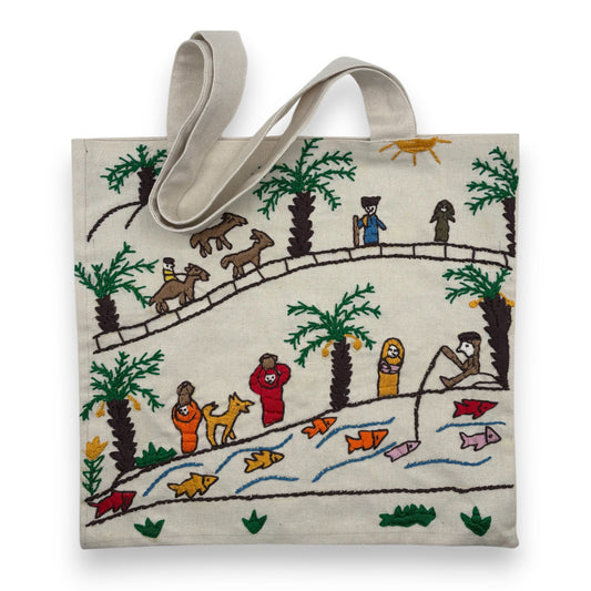 Off-white canvas tote bag with hand-embroidered design of people and animals on the bank of the Nile river