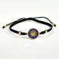 Black macrame bracelet with a brass medallion featuring a gold sun emblem on blue enamel