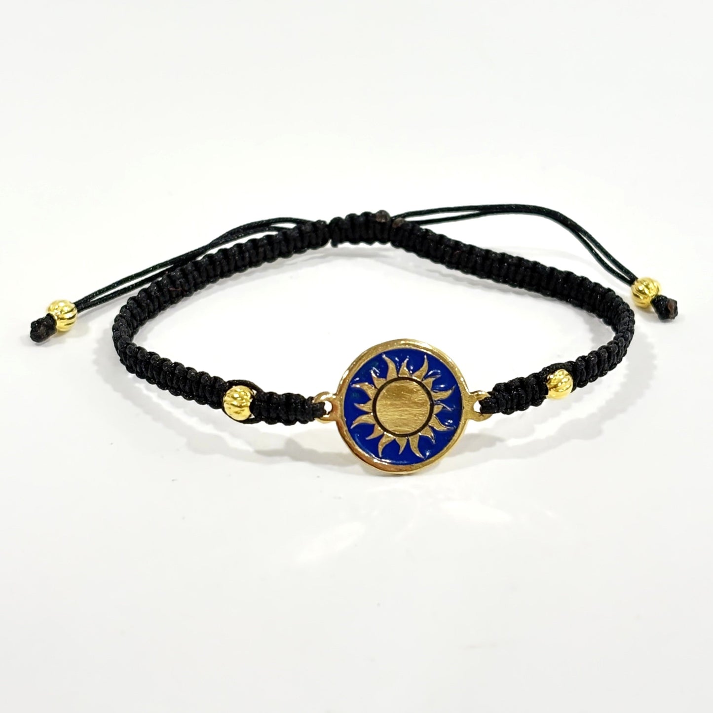 Black macrame bracelet with a brass medallion featuring a gold sun emblem on blue enamel