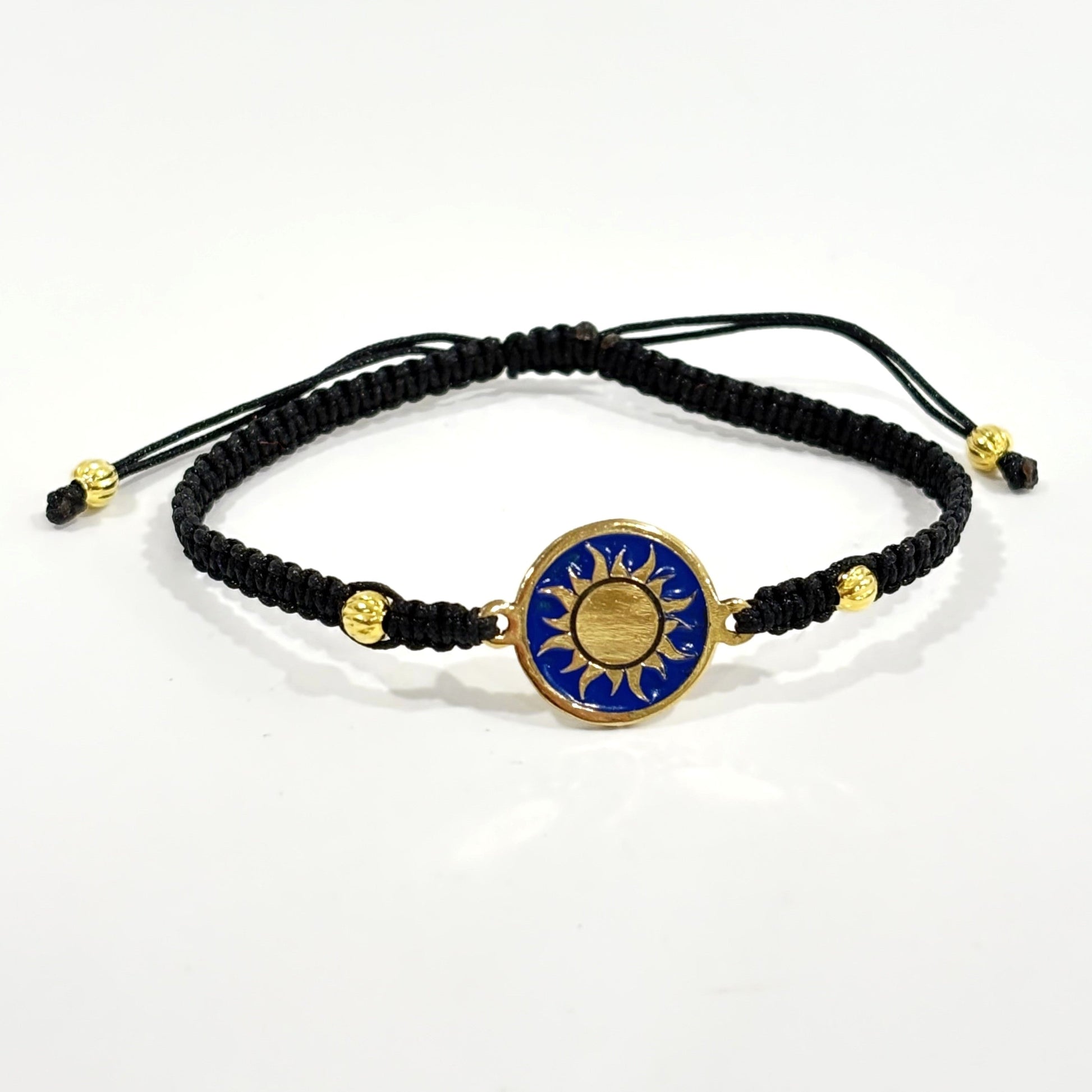Black macrame bracelet with a brass medallion featuring a gold sun emblem on blue enamel