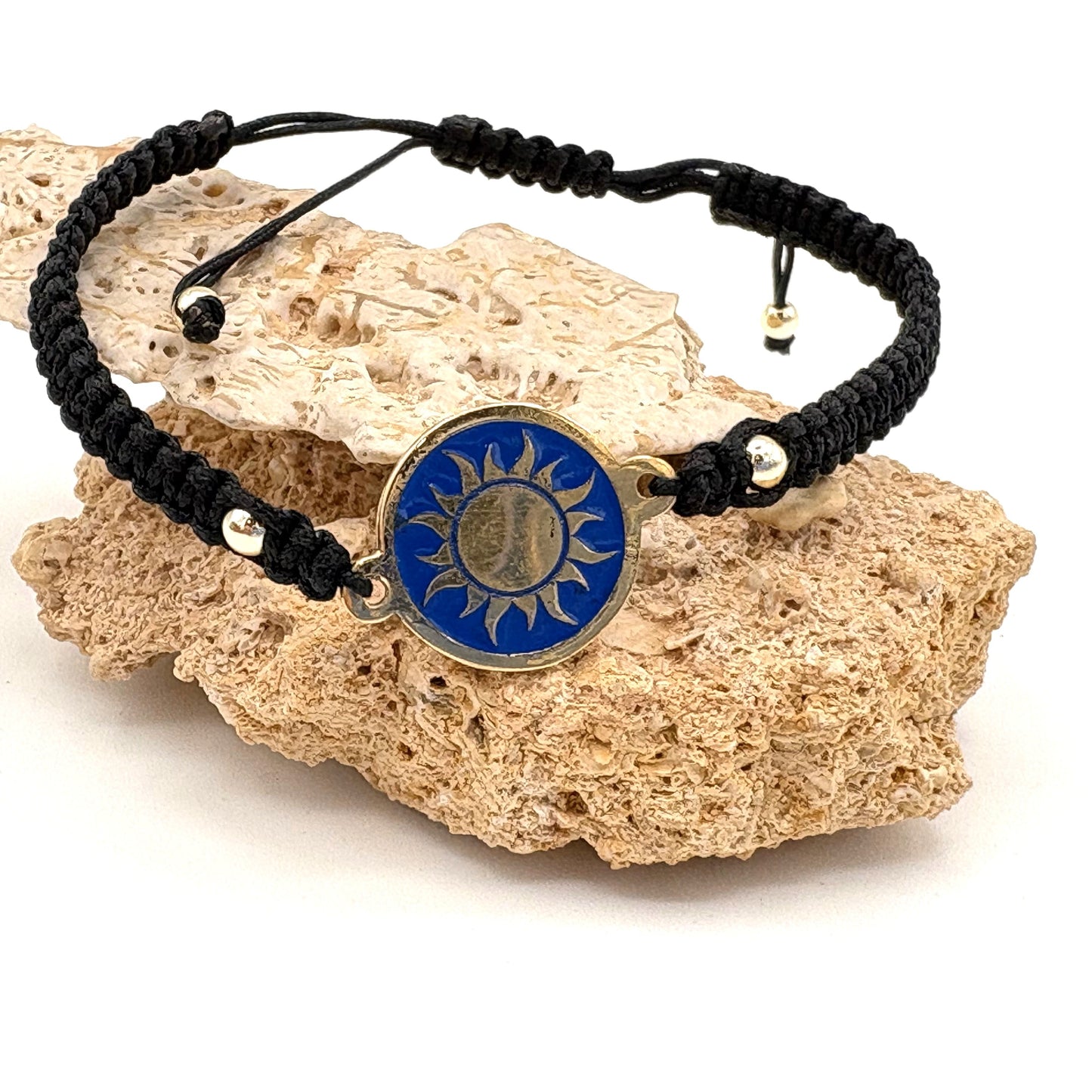 Black macrame bracelet with a brass medallion featuring a gold sun emblem on blue enamel