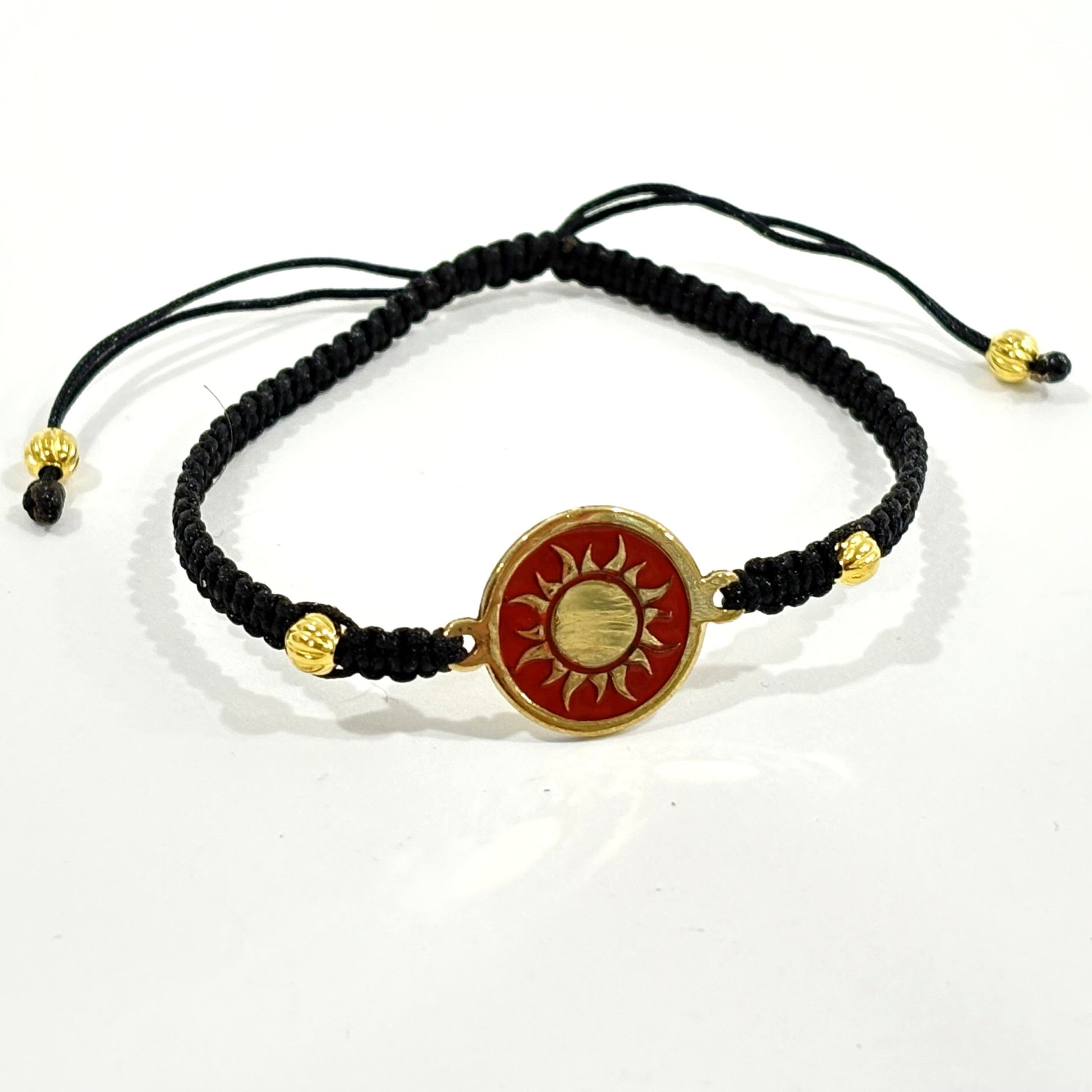Black macrame bracelet with a brass medallion featuring a gold sun emblem on maroon enamel
