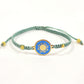 Teal macrame bracelet with a brass medallion featuring a gold sun emblem on turquoise enamel