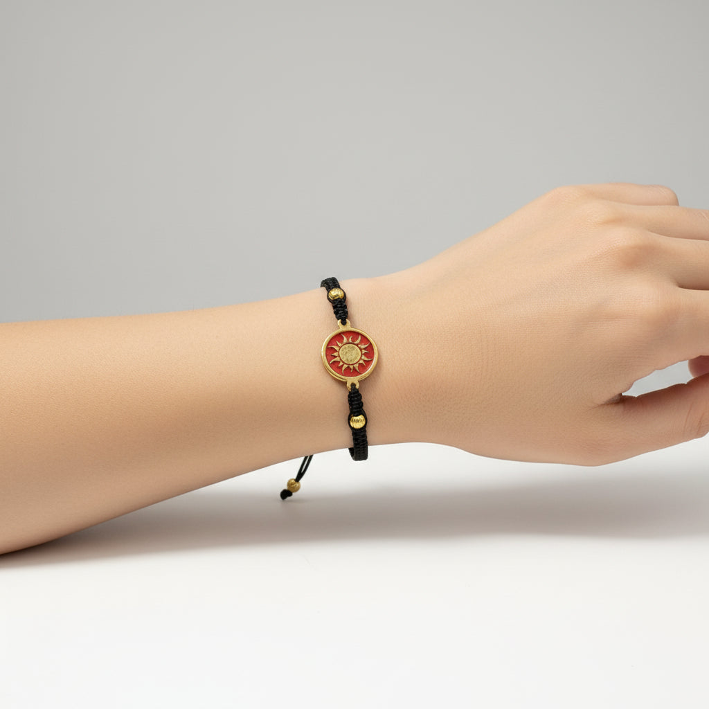 Black macrame bracelet with a brass medallion featuring a gold sun emblem on maroon enamel