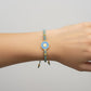 Teal macrame bracelet with a brass medallion featuring a gold sun emblem on turquoise enamel