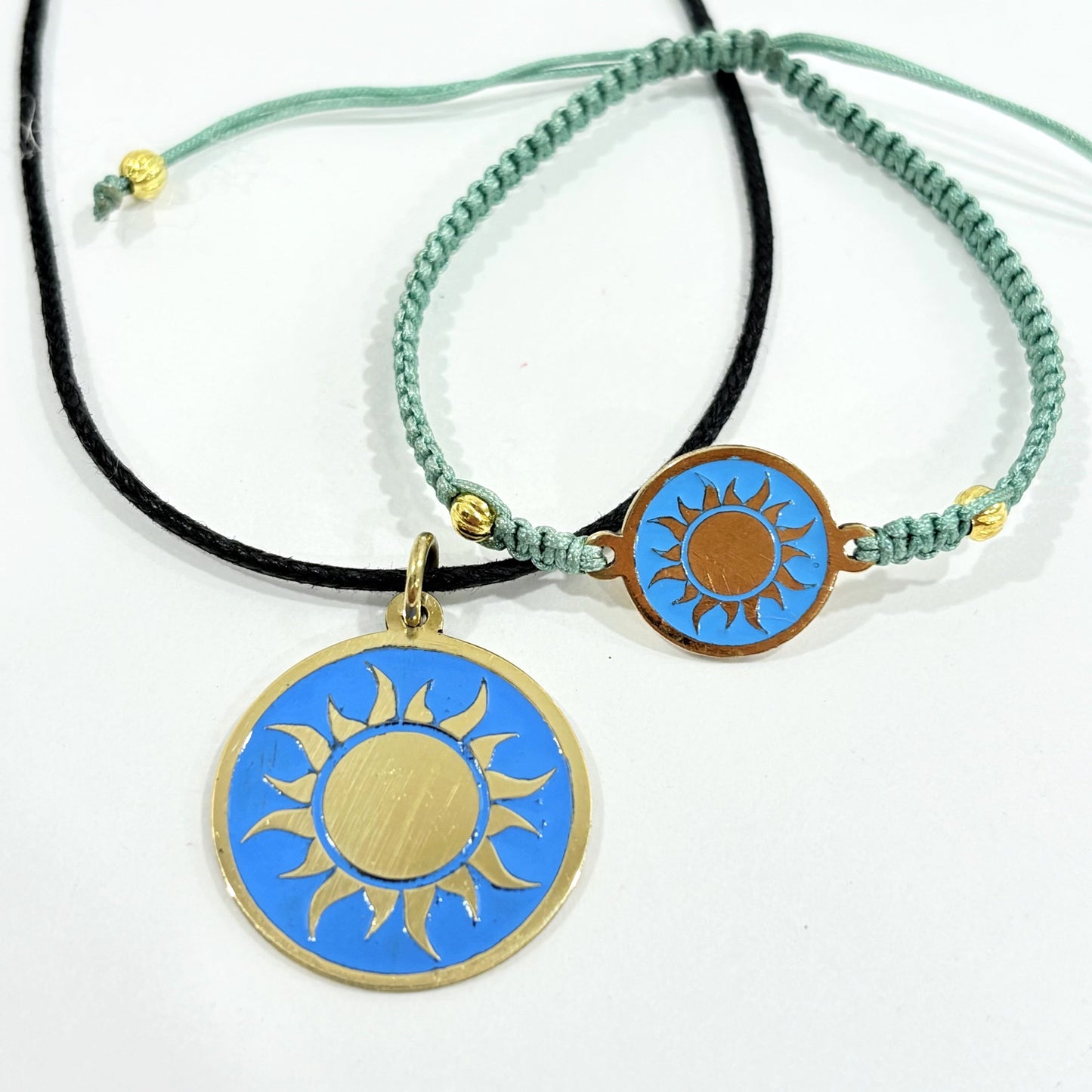 Teal macrame bracelet with a brass medallion featuring a gold sun emblem on turquoise enamel and matching pendant on black cord, fair trade handmade