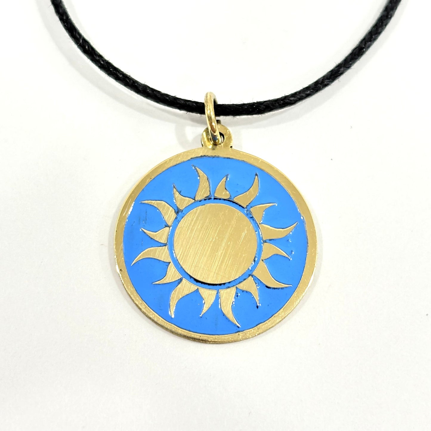 Handmade brass gold sun pendant on a turquoise blue enamel background with a black cord