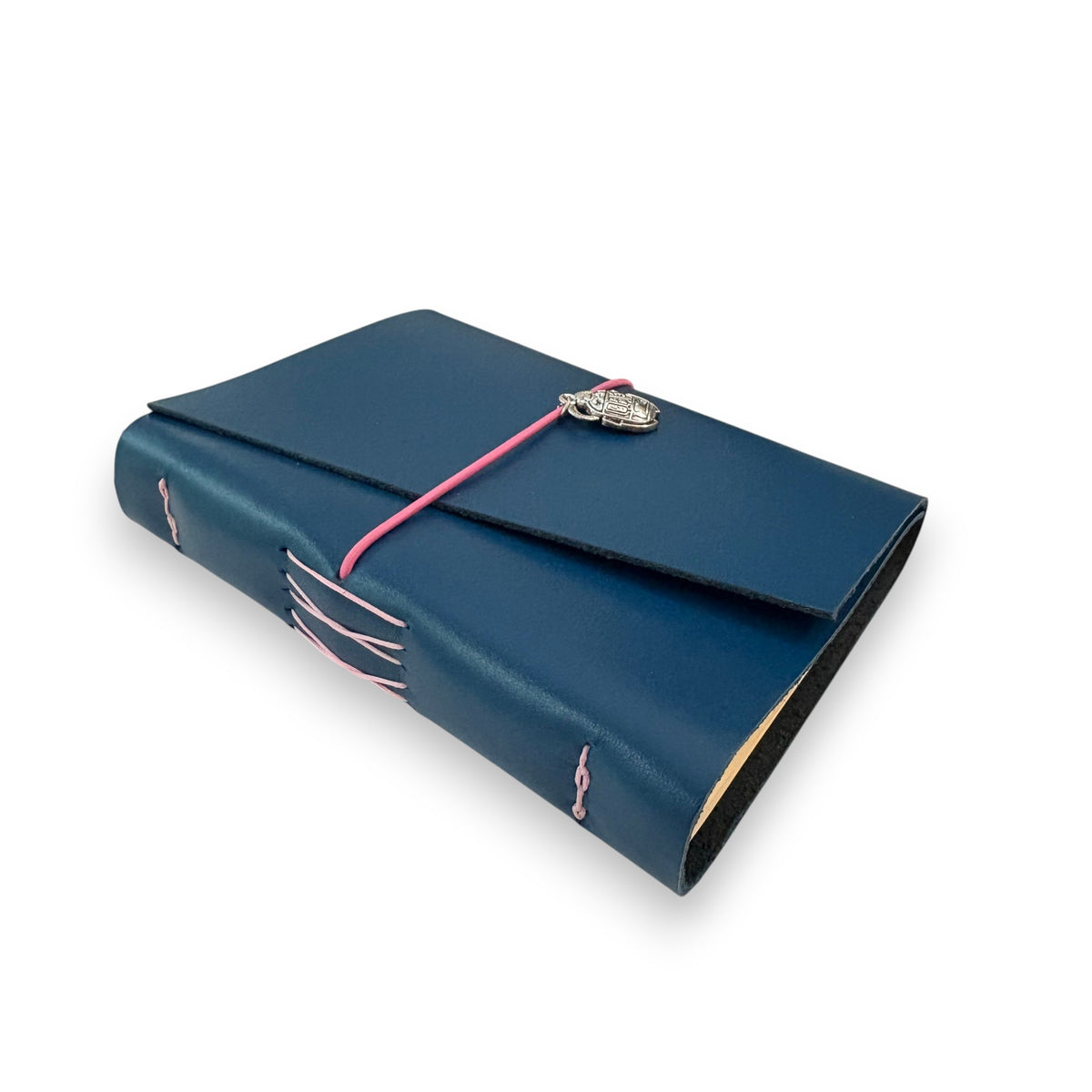 Handbound dark blue leather journal with a diagonal fold closure, secured by an elastic band featuring a silver scarab charm