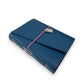Handbound dark blue leather journal with a diagonal fold closure, secured by an elastic band featuring a silver scarab charm