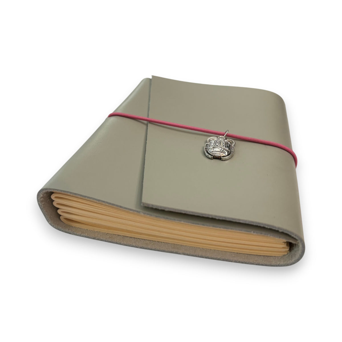 Gray handbound leather notebook with a diagonal fold design, wrapped with a pink elastic cord and featuring a silver-toned scarab charm