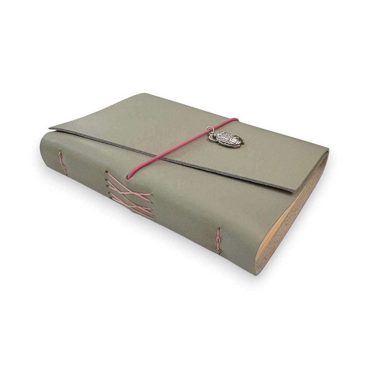 Gray handbound leather notebook with a diagonal fold design, wrapped with a pink elastic cord and featuring a silver-toned scarab charm