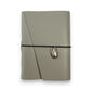 Gray handbound leather notebook with a diagonal fold design, wrapped with a pink elastic cord and featuring a silver-toned scarab charm