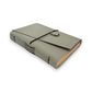 Gray handbound leather notebook with a diagonal fold design, wrapped with a pink elastic cord and featuring a silver-toned scarab charm