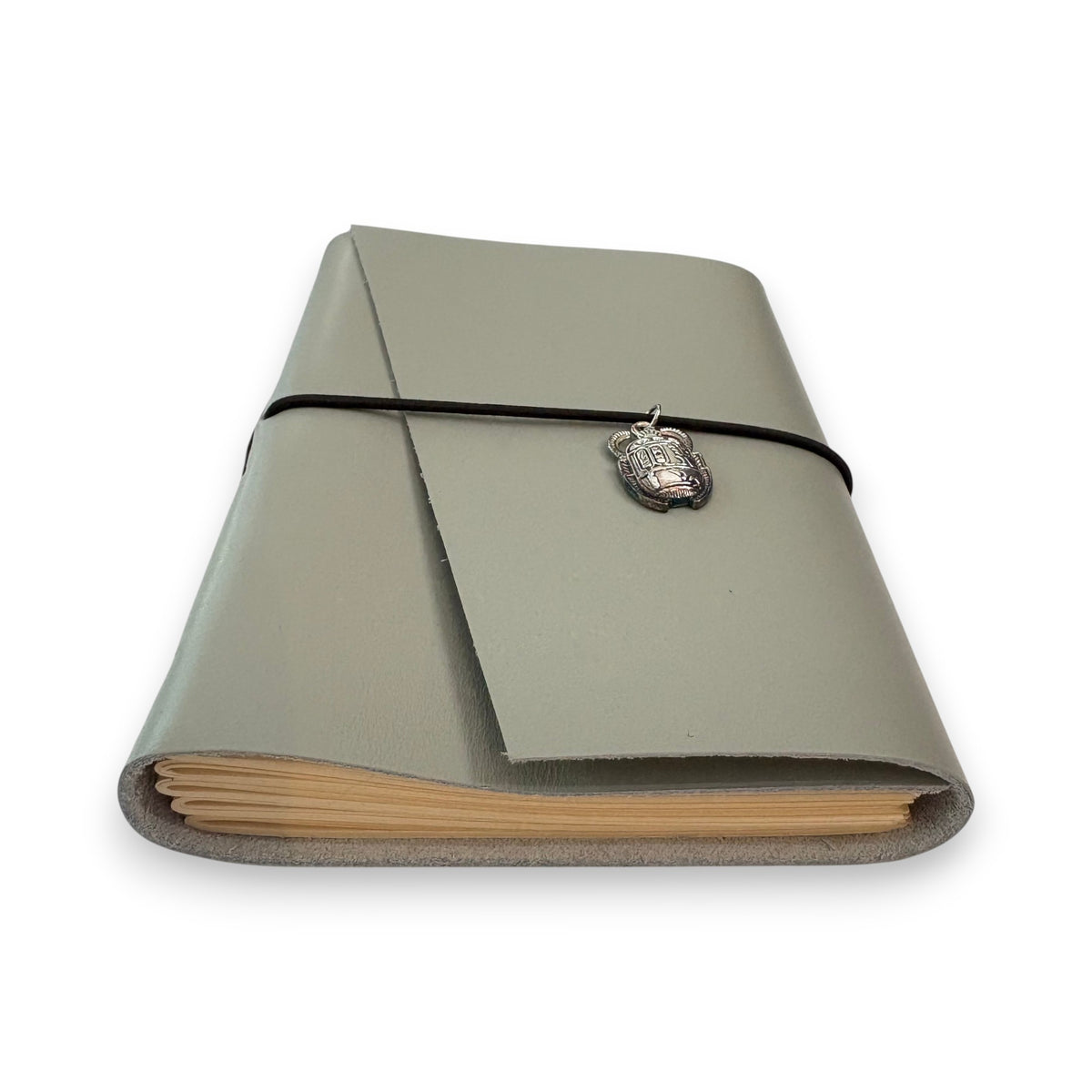 Gray handbound leather notebook with a diagonal fold design, wrapped with a pink elastic cord and featuring a silver-toned scarab charm