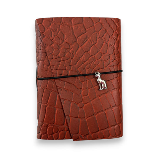 Rust red handbound leather journal with a wrap-around elastic strap and a silver metal cat goddess Bastet Charm