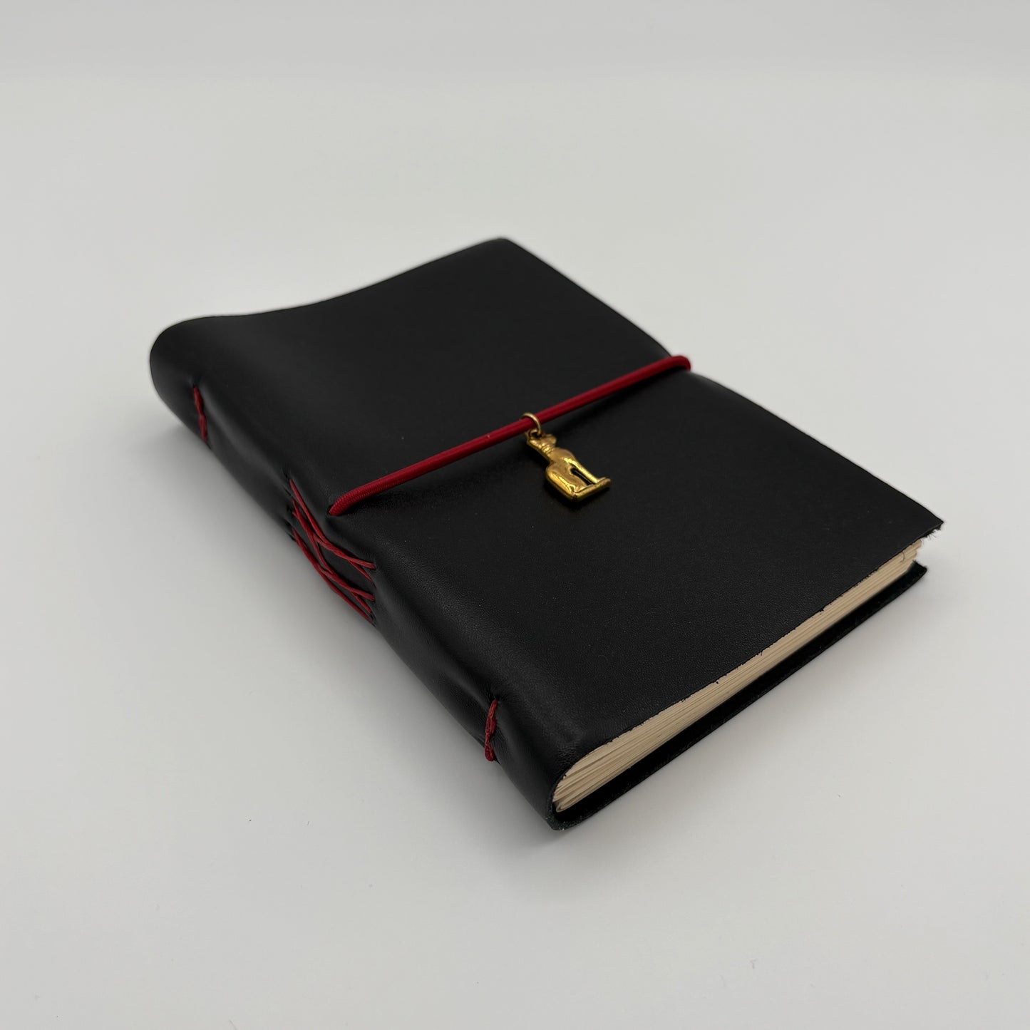 Handcrafted black leather journal with red string and gold Bastet cat charm, cruelty-free, fair trade, ethically handmade