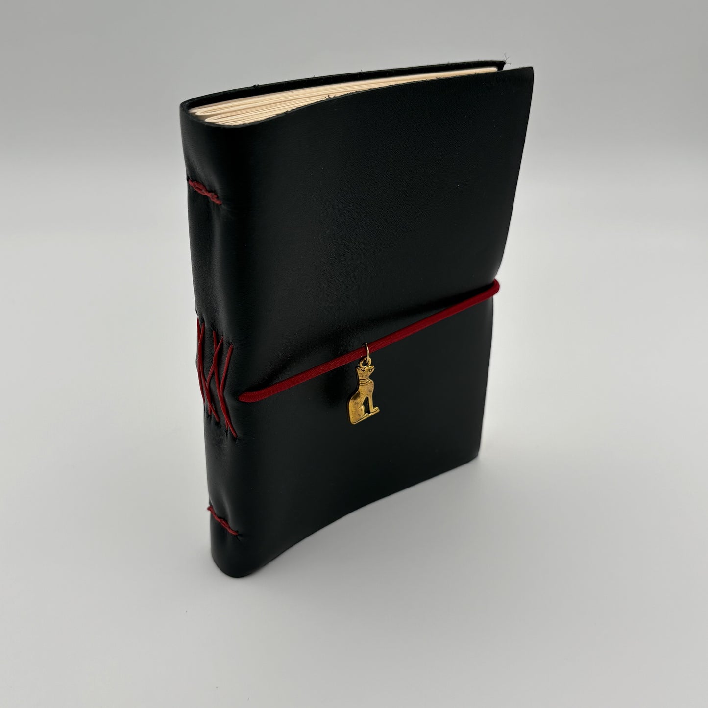 Handcrafted black leather journal with red string and gold Bastet cat charm, cruelty-free, fair trade, ethically handmade