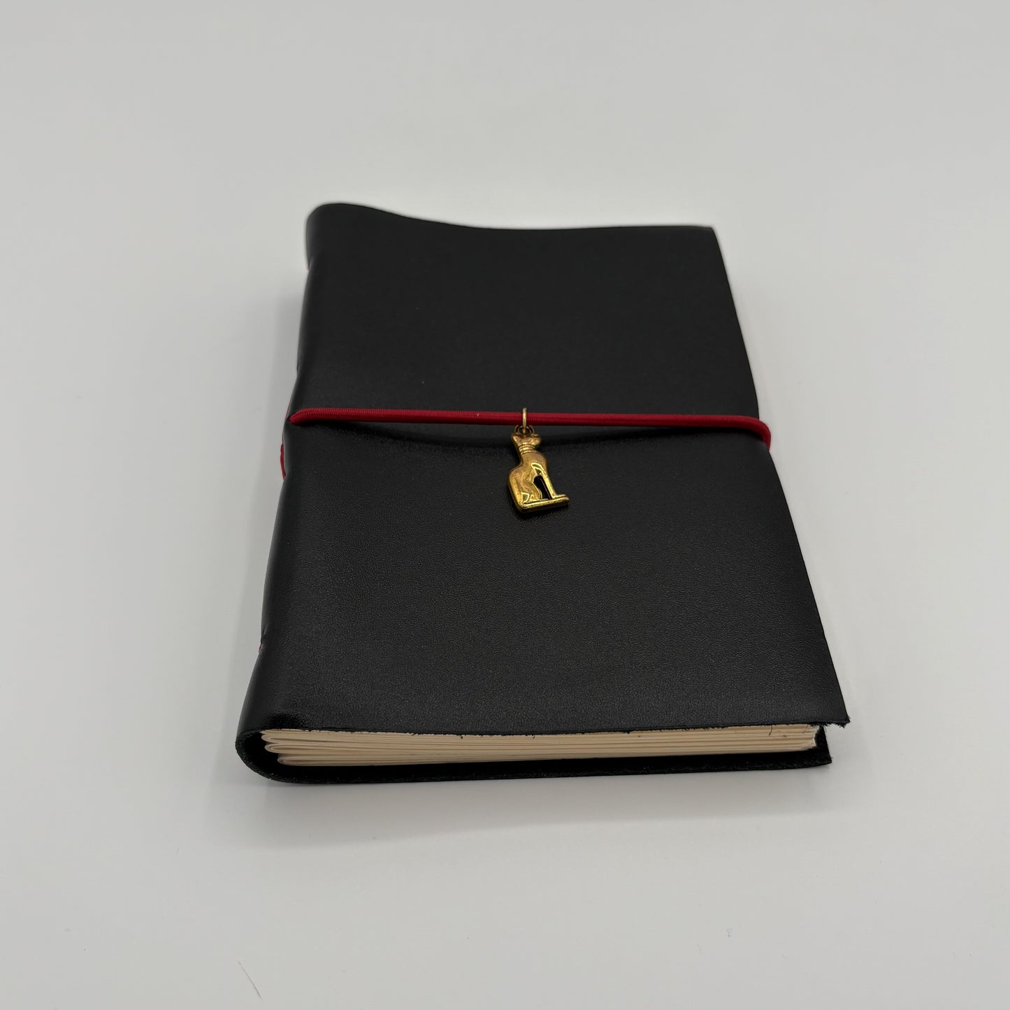 Handcrafted black leather journal with red string and gold Bastet cat charm, cruelty-free, fair trade, ethically handmade