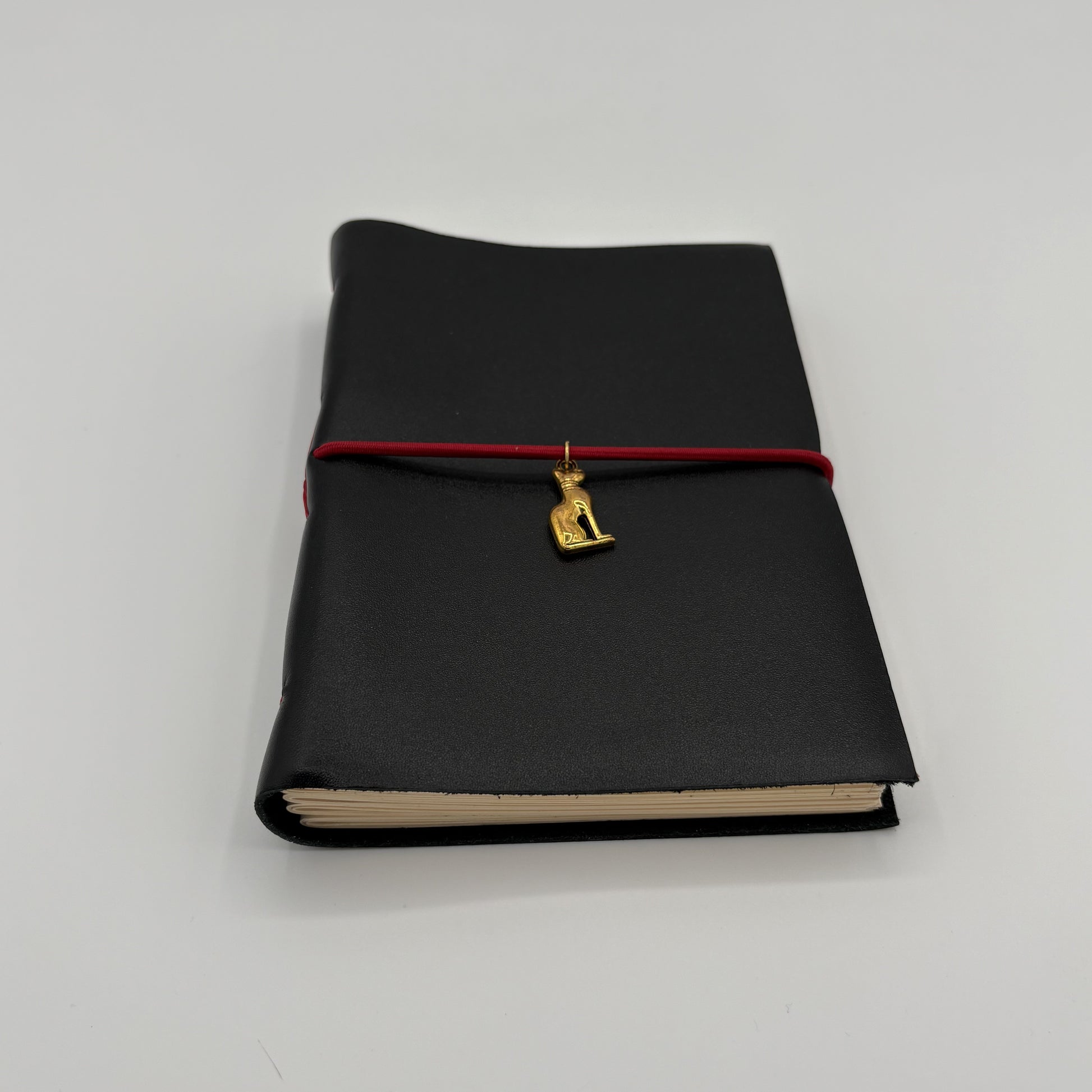 Handcrafted black leather journal with red string and gold Bastet cat charm, cruelty-free, fair trade, ethically handmade