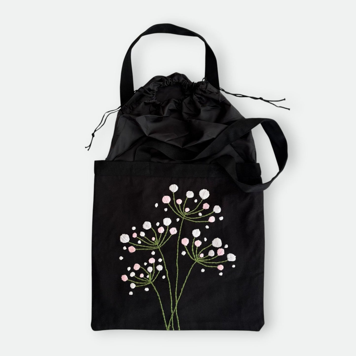 Handmade black tote bag with hand-embroidered white hydrangea and drawstring closure, fair trade