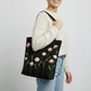 Handmade black tote bag with hand-embroidered pink and white marguerite, fair trade